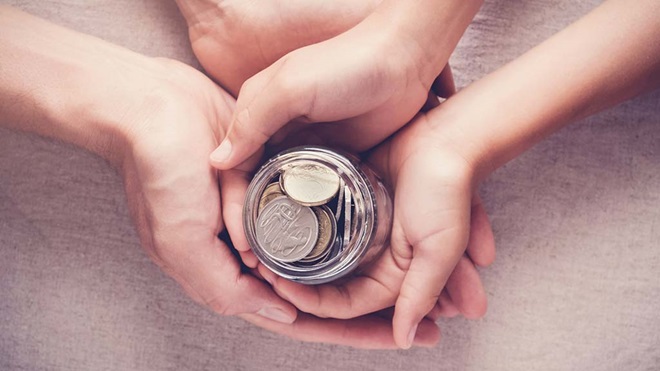 Hands of adult and child holding jar of coins
